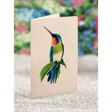 Load image into Gallery viewer, Card with a colorful hummingbird illustration on a textured surface with a blurred floral background